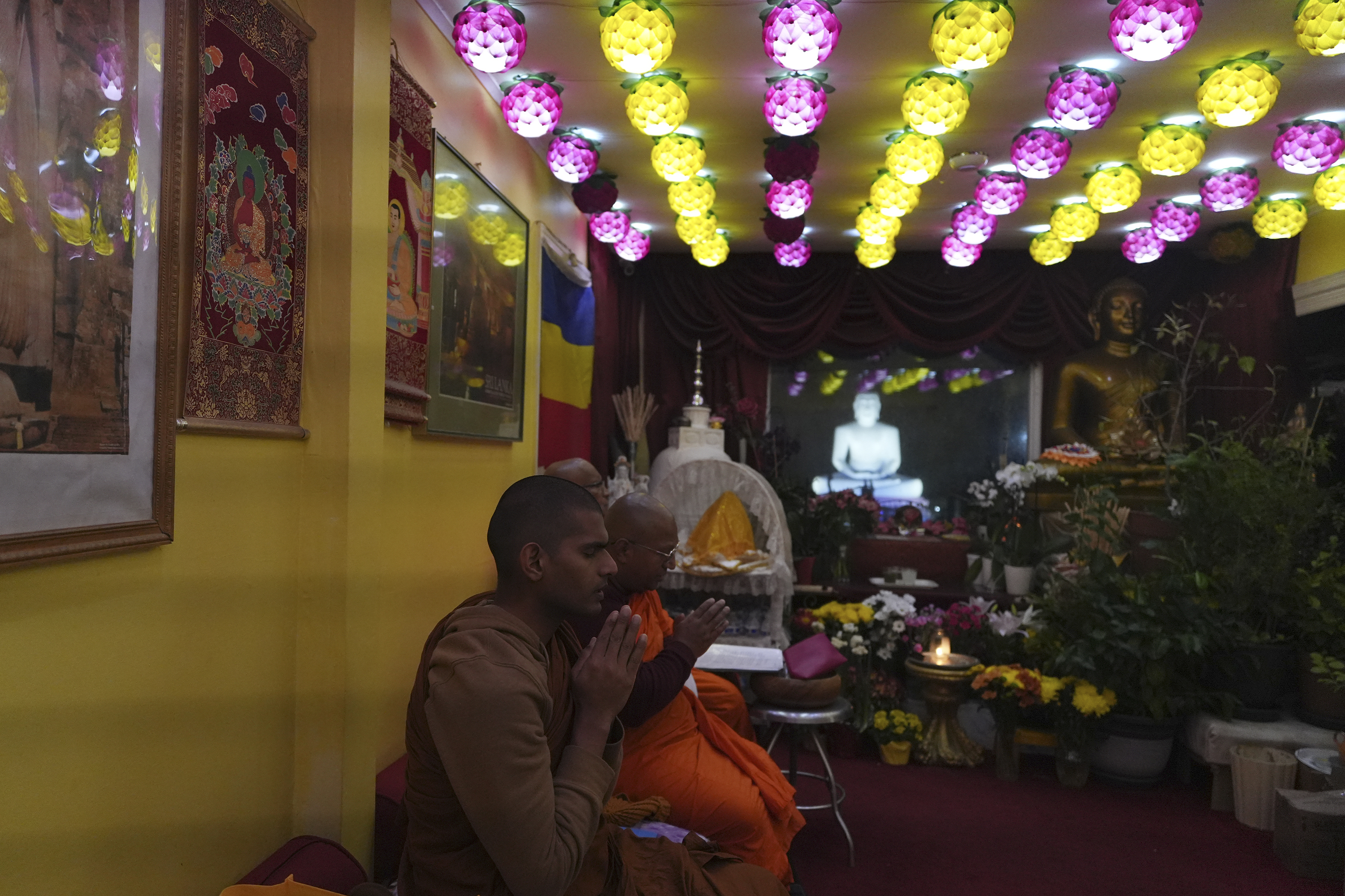 Monks chant sutras in Pāli language next to a flowered-decorated altar overlooking a giant Buddha statue in the yard of the New Jersey Buddhist Vihara and Meditation Center in Franklin Township, N.J. on Sunday Nov. 30, 2024. (AP photo/Luis Andres Henao)